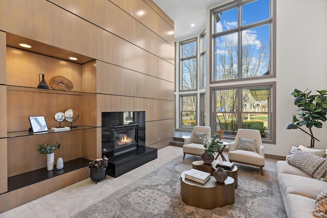 living room with baseboards, carpet flooring, recessed lighting, a towering ceiling, and a glass covered fireplace