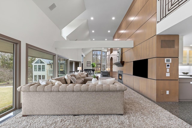 living area featuring a glass covered fireplace, recessed lighting, and high vaulted ceiling