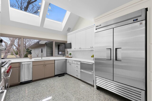 kitchen with vaulted ceiling with skylight, a sink, decorative backsplash, light countertops, and appliances with stainless steel finishes