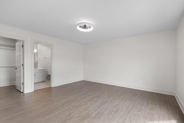 unfurnished bedroom featuring a walk in closet, dark wood-type flooring, ensuite bath, a closet, and baseboards