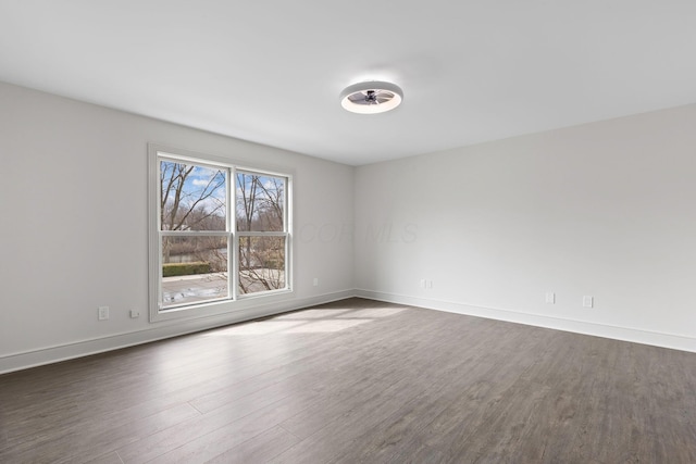 spare room with baseboards and dark wood finished floors