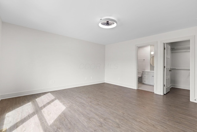 unfurnished bedroom with ensuite bathroom, a walk in closet, baseboards, and dark wood-style flooring