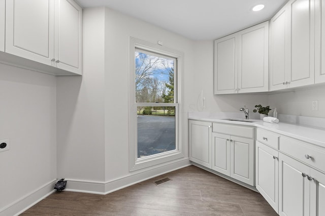 laundry room with a sink, cabinet space, light wood-style floors, baseboards, and hookup for an electric dryer