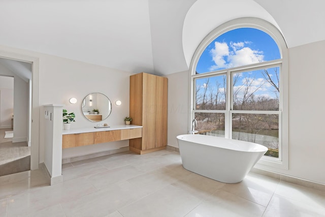 full bathroom featuring tile patterned floors, lofted ceiling, baseboards, a freestanding bath, and vanity