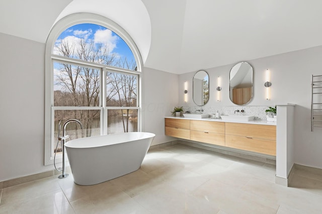 bathroom with double vanity, lofted ceiling, a sink, a freestanding bath, and tasteful backsplash