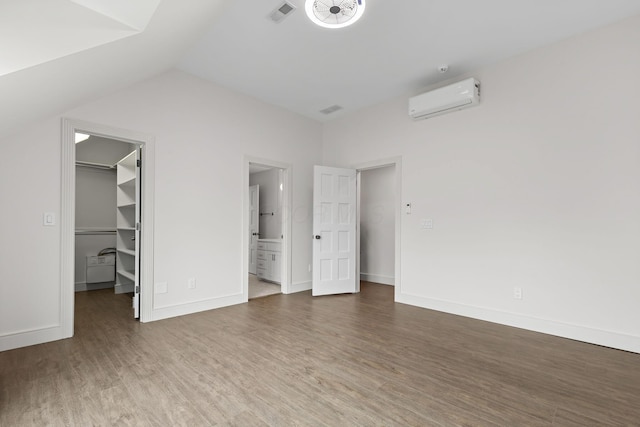 unfurnished bedroom featuring visible vents, a walk in closet, baseboards, a wall mounted air conditioner, and wood finished floors