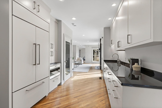 kitchen featuring dark countertops, a sink, recessed lighting, light wood-style floors, and built in fridge