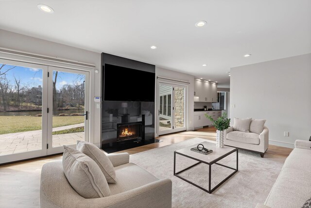 living area with recessed lighting, light wood-style floors, and a warm lit fireplace