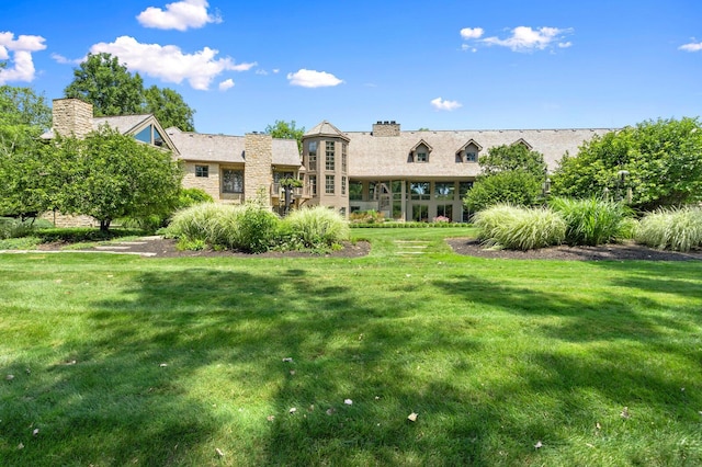 back of property featuring a lawn, stone siding, and a chimney