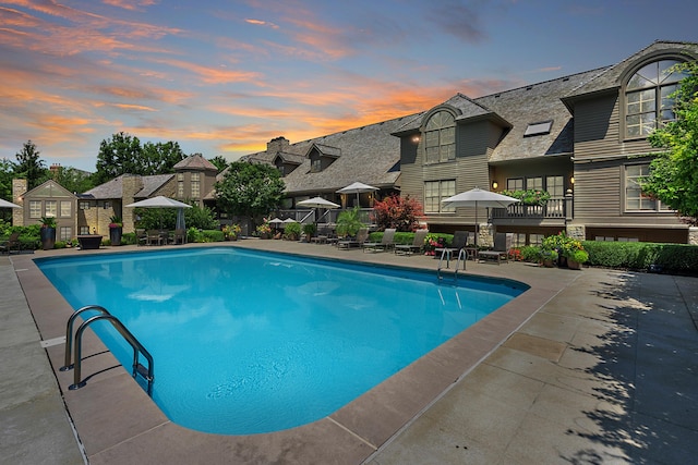 pool at dusk with a patio area, a fenced in pool, and a residential view