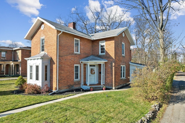 view of front of property featuring a front yard, brick siding, and a chimney