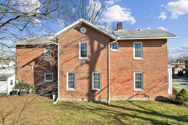 rear view of house with central air condition unit, a yard, crawl space, brick siding, and a chimney