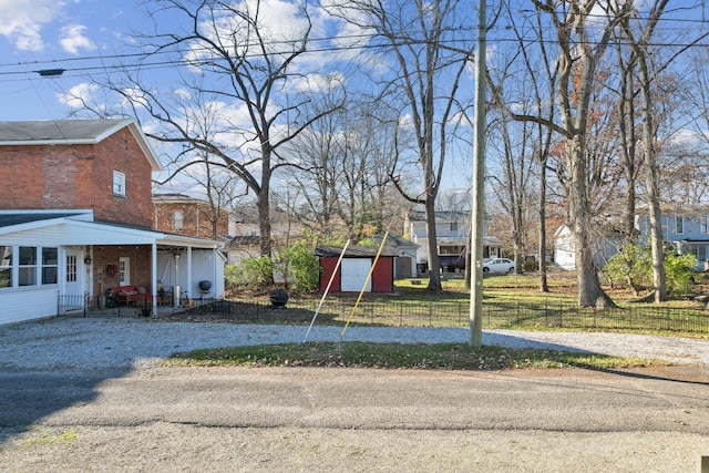 view of yard featuring a storage unit, an outdoor structure, driveway, and fence