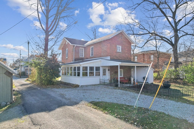 view of front of house featuring brick siding, fence, driveway, and a sunroom