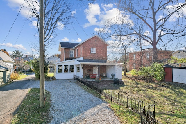 traditional-style house featuring an outbuilding, fence, gravel driveway, a storage shed, and brick siding