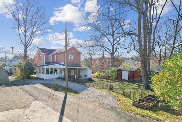 view of front of house featuring brick siding, a fenced front yard, an outbuilding, driveway, and a vegetable garden