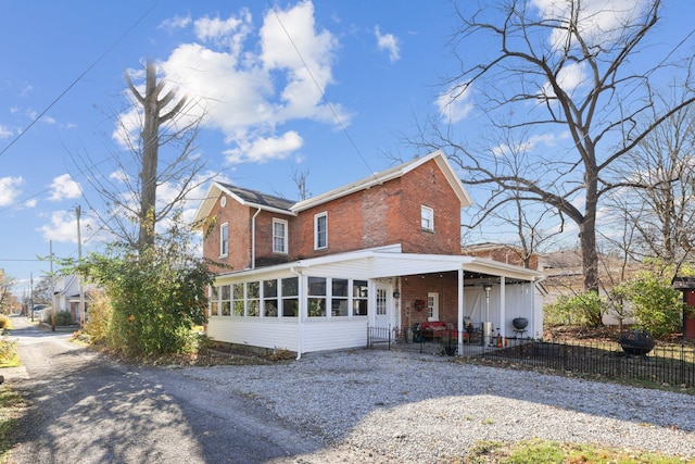 view of front of home with brick siding, gravel driveway, fence, and a sunroom