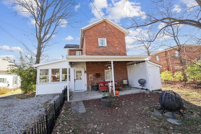 traditional home with fence, a fire pit, brick siding, and a sunroom