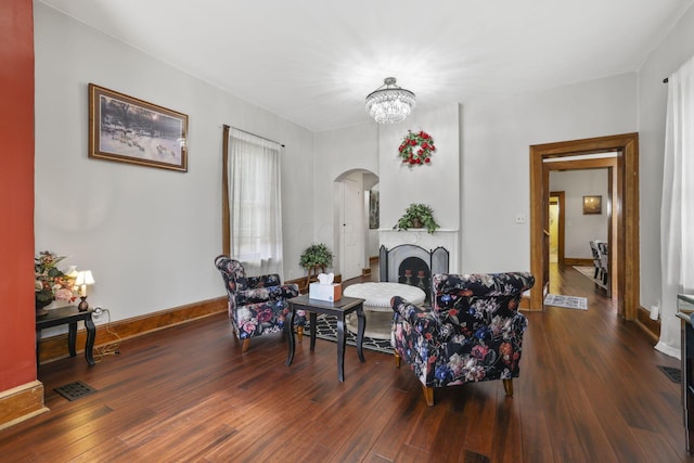 living room with baseboards, a fireplace, hardwood / wood-style flooring, arched walkways, and a notable chandelier