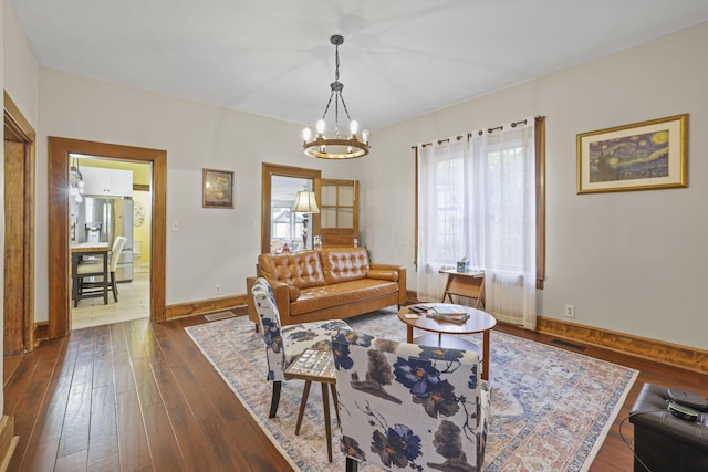 living room featuring dark wood-style floors, visible vents, baseboards, and an inviting chandelier