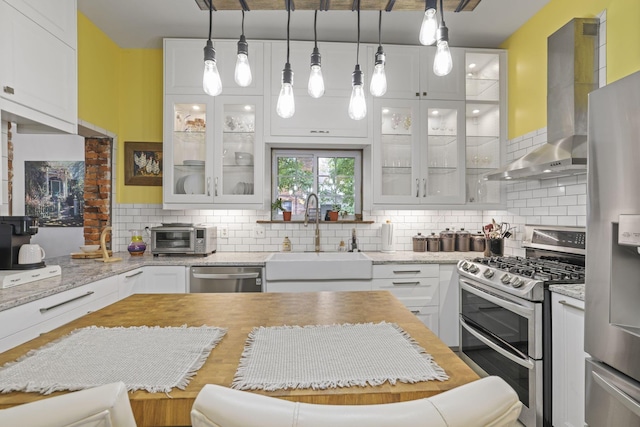 kitchen with light stone countertops, a sink, stainless steel appliances, wall chimney range hood, and backsplash