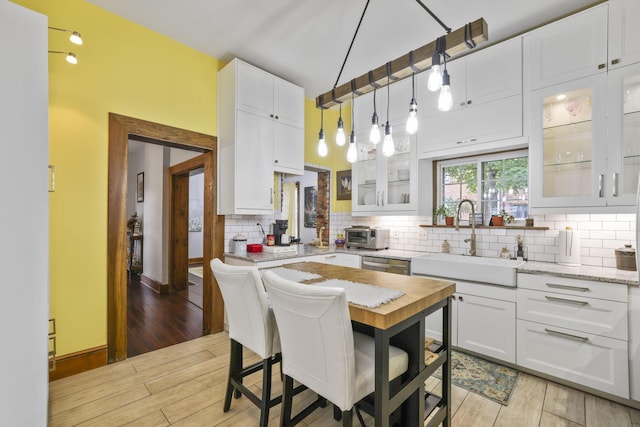 kitchen featuring tasteful backsplash, white cabinets, light wood-style floors, and a sink