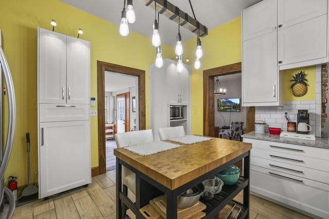 kitchen featuring wood finish floors, decorative light fixtures, stainless steel microwave, white cabinetry, and decorative backsplash