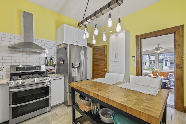 kitchen featuring white cabinets, light wood-style floors, appliances with stainless steel finishes, wall chimney range hood, and backsplash