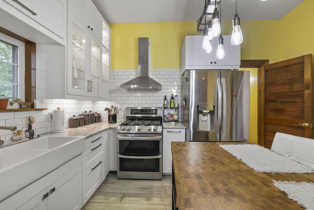 kitchen featuring butcher block countertops, appliances with stainless steel finishes, wall chimney exhaust hood, white cabinets, and decorative backsplash