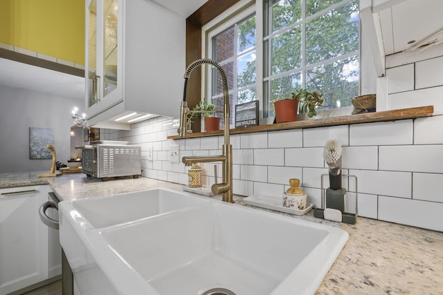 kitchen featuring a sink, light stone counters, backsplash, and white cabinets