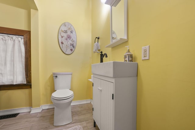 bathroom featuring baseboards, toilet, wood finished floors, and vanity