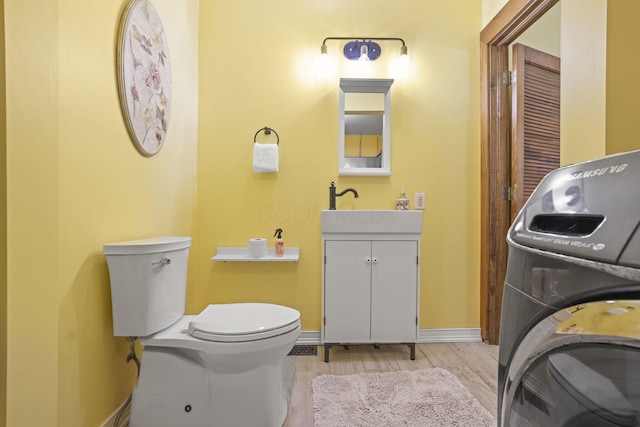 bathroom featuring baseboards, toilet, washer / dryer, wood finished floors, and vanity