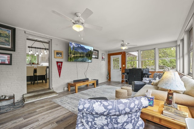 living room with ceiling fan, wood finished floors, and brick wall