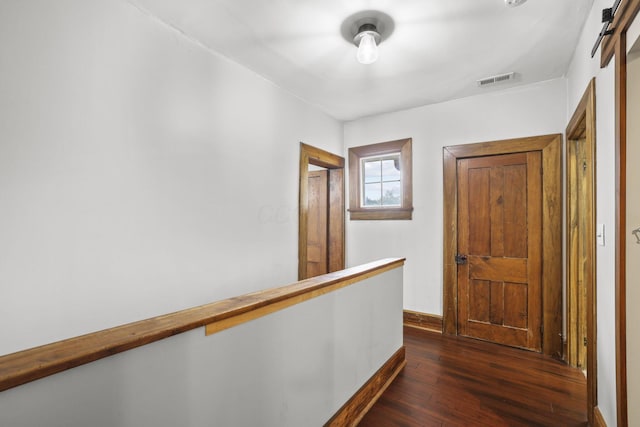 hall with visible vents, dark wood-type flooring, baseboards, a barn door, and an upstairs landing