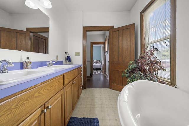 ensuite bathroom with a soaking tub, double vanity, tile patterned floors, and a sink