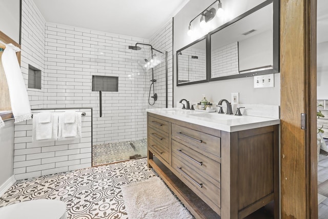 full bath featuring a sink, visible vents, tiled shower, and double vanity