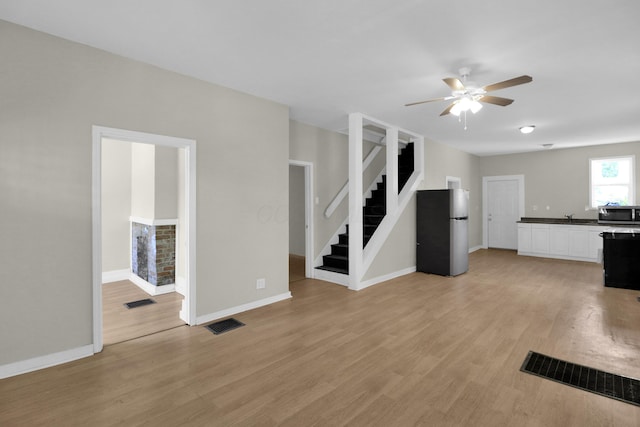 unfurnished living room with light wood-type flooring, visible vents, and stairway