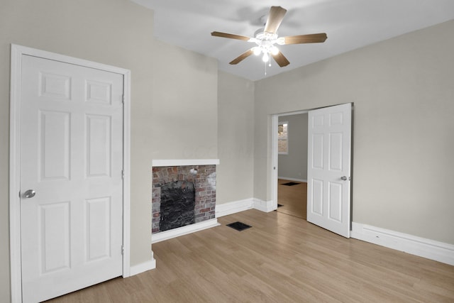 unfurnished living room with light wood finished floors, visible vents, a brick fireplace, ceiling fan, and baseboards