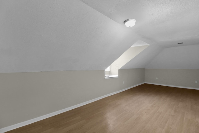 additional living space with a textured ceiling, baseboards, and wood finished floors