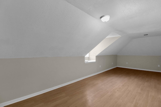 bonus room with baseboards, a textured ceiling, vaulted ceiling, and light wood-style floors