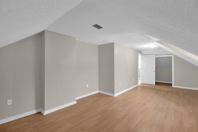 additional living space featuring baseboards, visible vents, vaulted ceiling, a textured ceiling, and light wood-type flooring