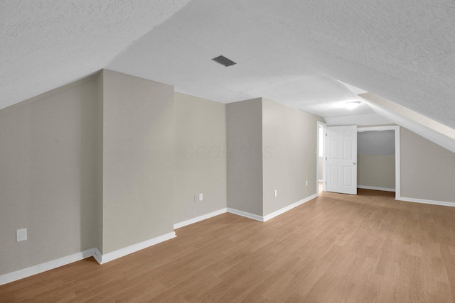 additional living space featuring a textured ceiling, light wood-style flooring, visible vents, baseboards, and vaulted ceiling