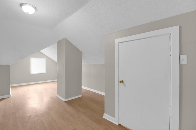 additional living space featuring lofted ceiling, a textured ceiling, baseboards, and wood finished floors