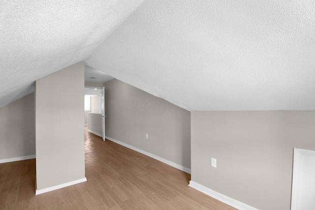 bonus room with lofted ceiling, a textured ceiling, wood finished floors, and baseboards