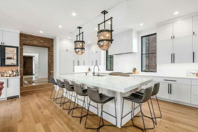 kitchen featuring brick wall, a breakfast bar area, light wood-type flooring, and white cabinets