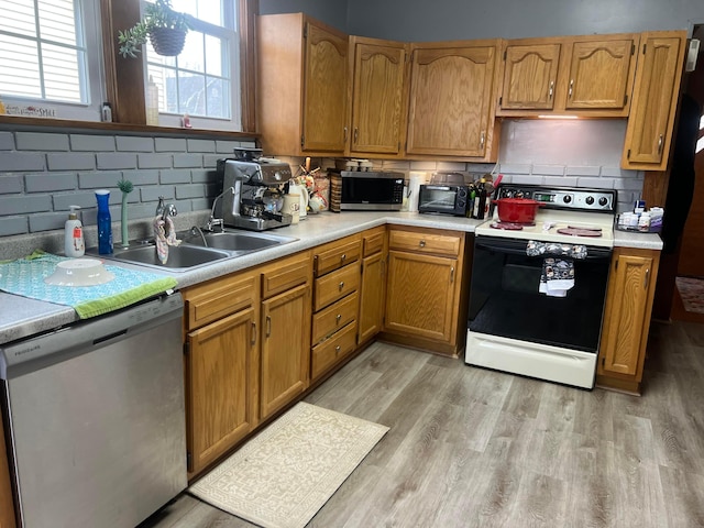 kitchen with stainless steel appliances, a sink, light countertops, and light wood-style floors