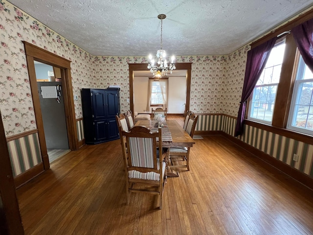 dining space with wallpapered walls, wainscoting, wood-type flooring, a textured ceiling, and a chandelier