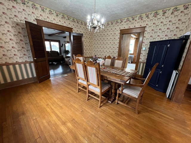 dining room featuring a wainscoted wall, a textured ceiling, light wood-type flooring, and wallpapered walls