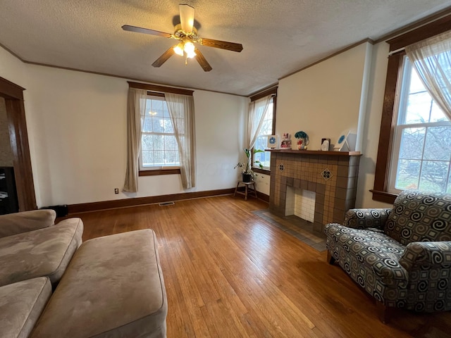 living room featuring ornamental molding, plenty of natural light, a tiled fireplace, and wood finished floors