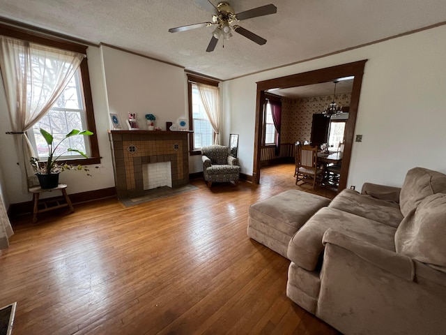 living area featuring baseboards, a tiled fireplace, ornamental molding, hardwood / wood-style floors, and a textured ceiling